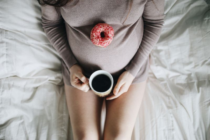 zwangere vrouw op bed met donut en koffie